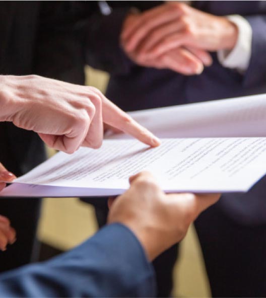 Close-up of a person in a suit gesturing towards a document held by another individual, highlighting an engaging discussion or review. Hands are emphasized, illustrating collaboration as they interact with the paper's content.